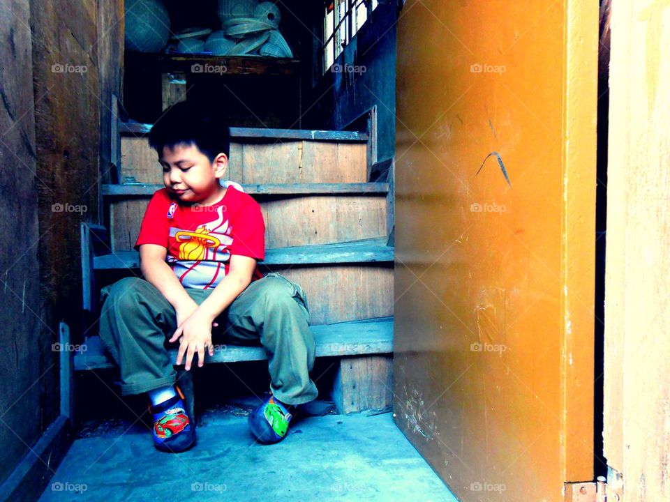 Young asian kid sitting by the steps of a staircase by a doorstep