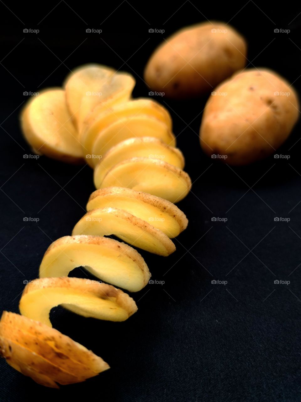 Spiral sliced ​​potatoes and two whole potatoes.  Black background