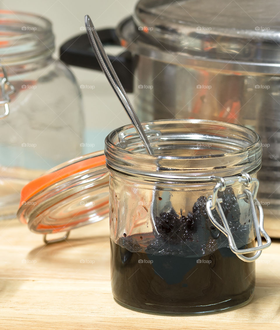 A half filled jar of mulberry liqueur with a spoon.
