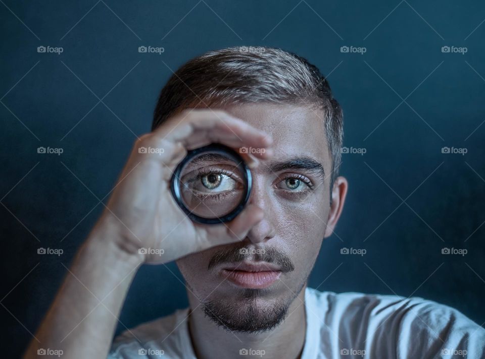 Close-up portrait of young man looking through magnifying glass .