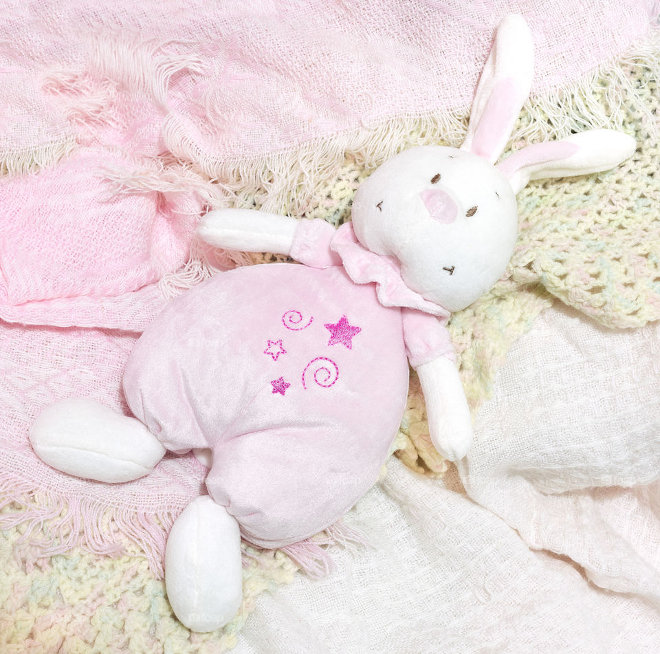 A soft pink plush rabbit baby toy on a pink baby shawl.