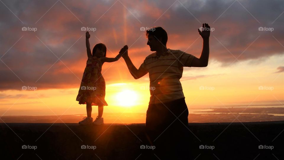 Father with her daughter raising arms at sunset