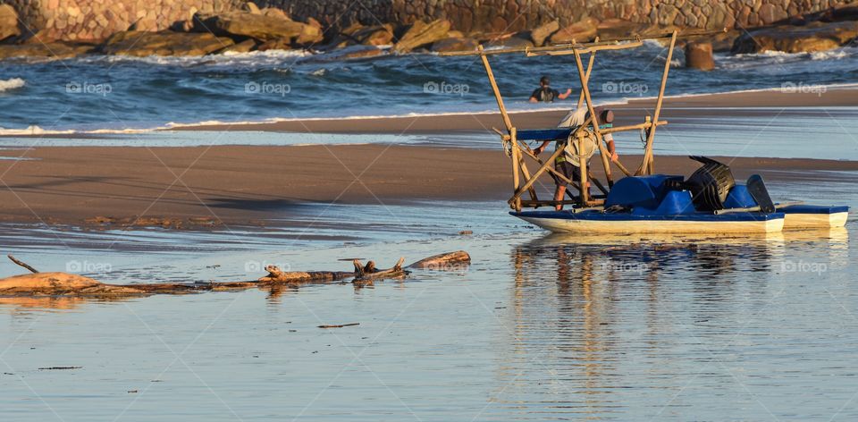 Golden hour is fast approaching over a deserted beach in South Africa, lonely fisherman packing up his gear for the day in shallow lagoon water next to the beach sand