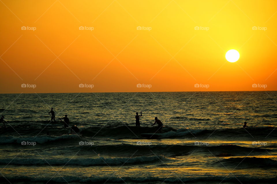 surfing at golden hour. people surfing at sunset in the beach