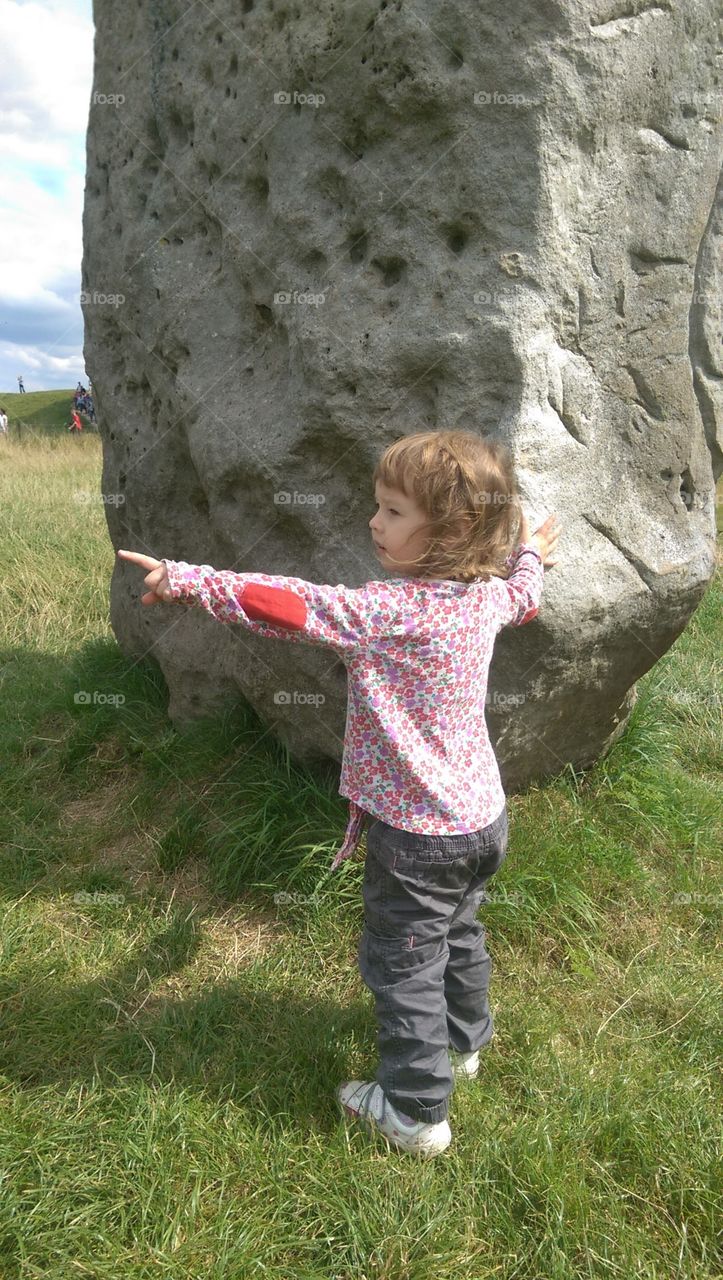 child standing by prehistoric stone in summer pointing into distance