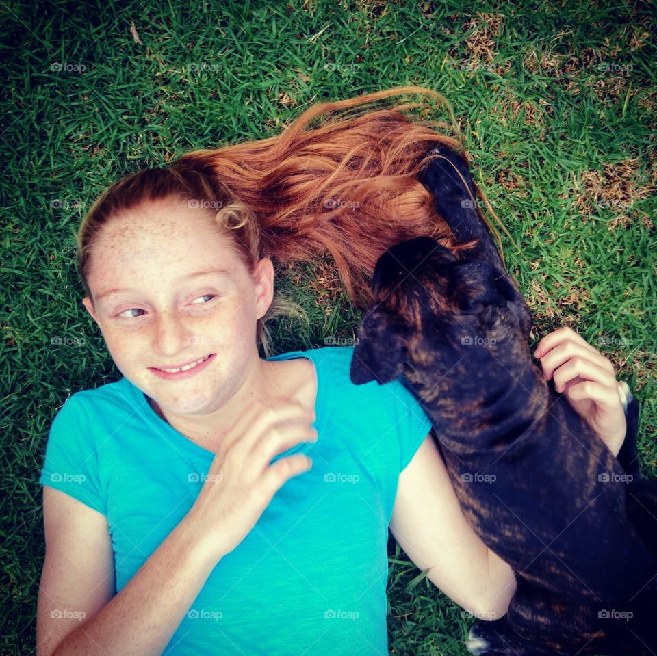 strawberry secrets. Smiling redhead girl lying on her back playing with brindle Boxer puppy.