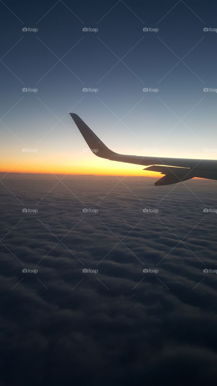 Airplane flying above clouds during sunset
