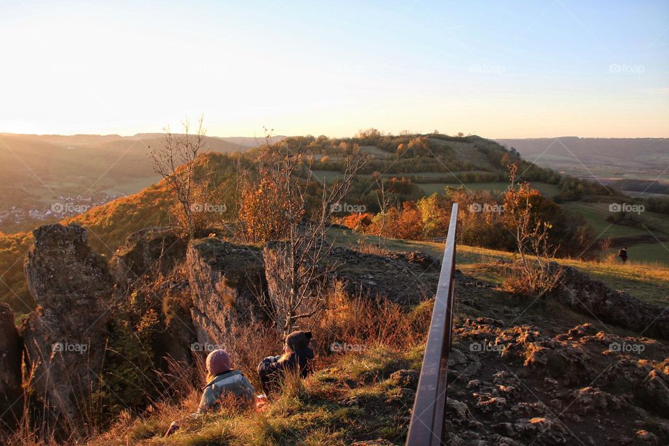 Two women sit together on a mountain in the grass to watch the sunrise in autumn