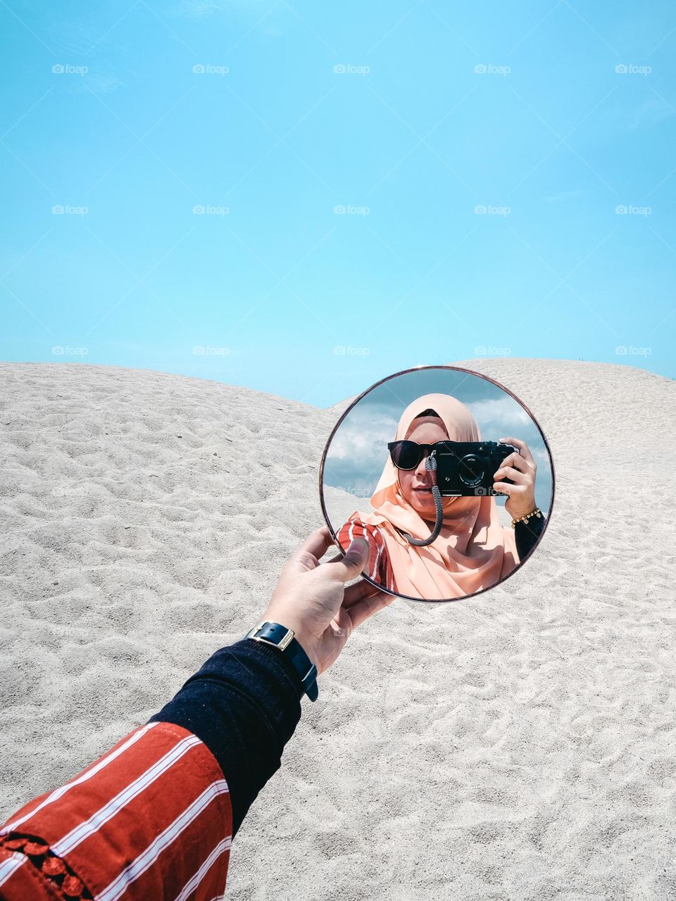 A woman taking a selfie with a mirror with sand dunes background