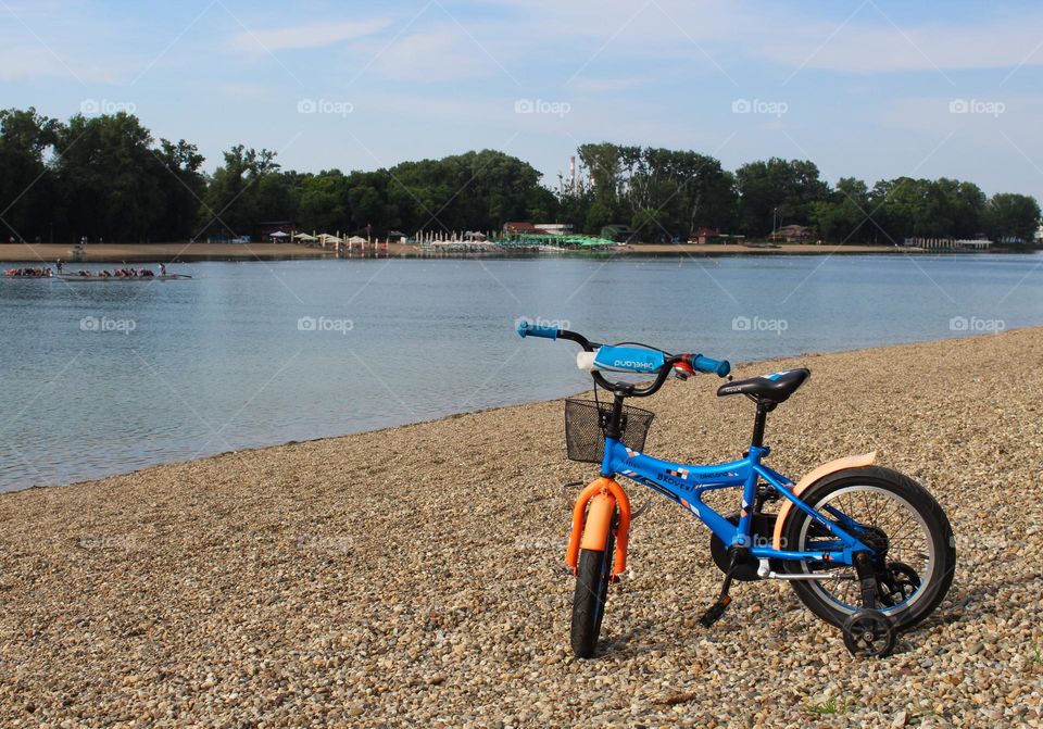 One blue-orange lonely children's bicycle on the shore by the lake.  Spring landscape