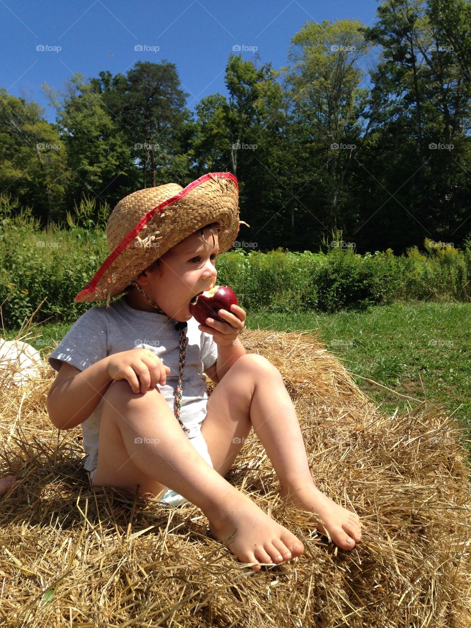 View of young boy sitting on hay eating apple