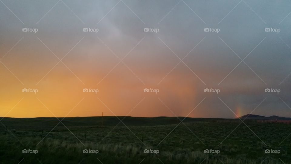 Sunset highlights a rain cloud and creates a rainbow on the horizon