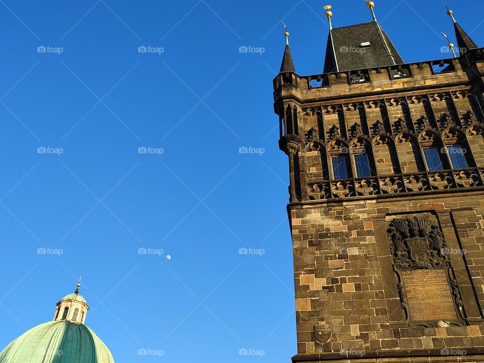 Moon on the day blue sky along with the Old Town Bridge Tower in Prague.