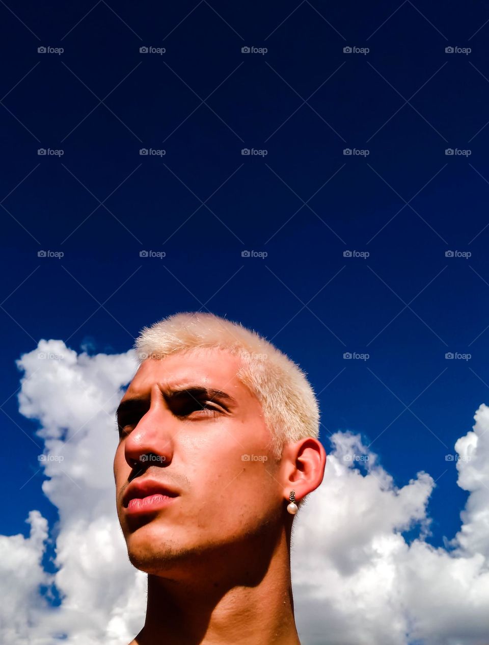 eautiful Selfie Portrait of a blonde man, with an earring, with a gorgeous blue sky and fluffy white clouds on the background