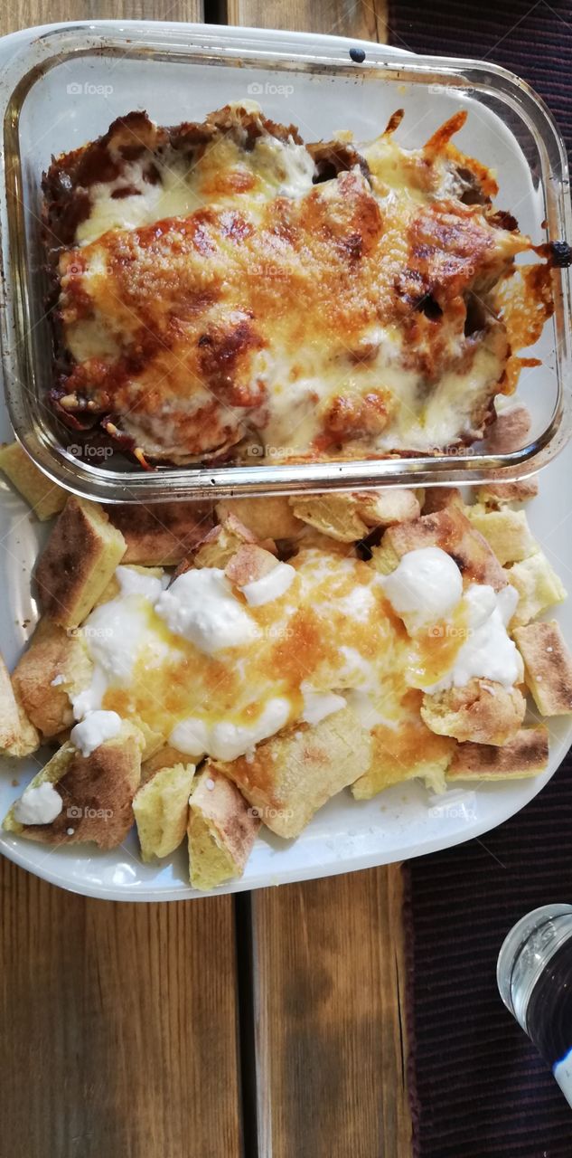 In the glass bowl a portion of kebab, cheese on the top. The pieces of the bread with yoghurt and garlic on the plate.