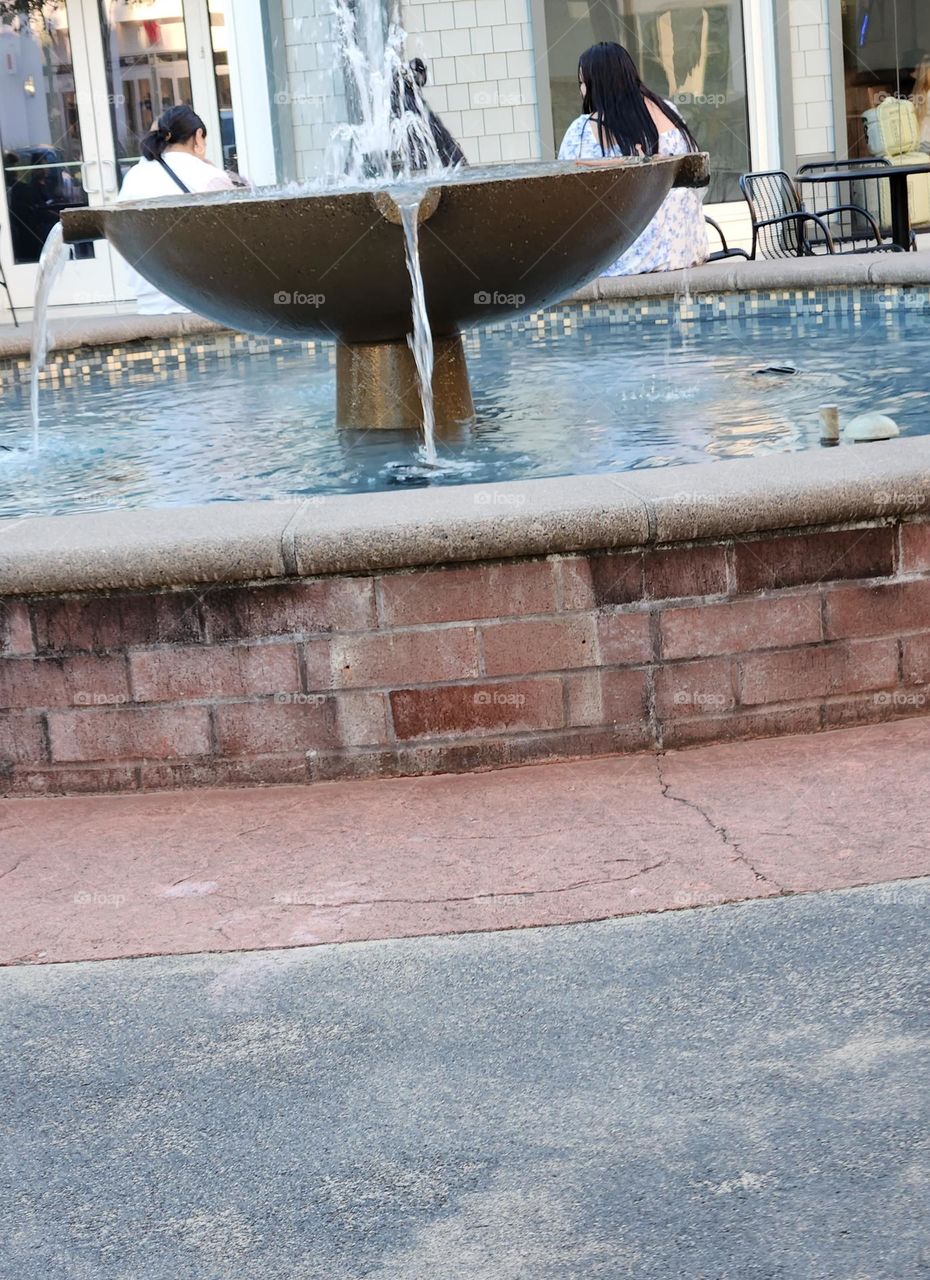 two women sitting by a fountain to cool off in an outdoor shopping center court on a hot Summer evening in Oregon