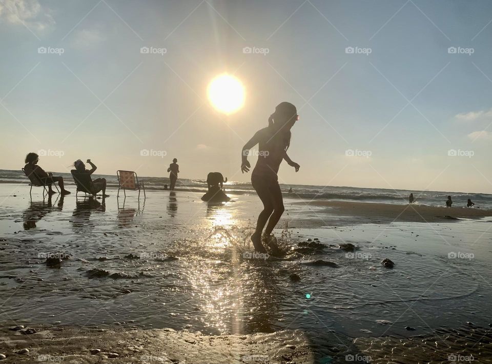 Girl jumping in surf water with big sun on background before sunset