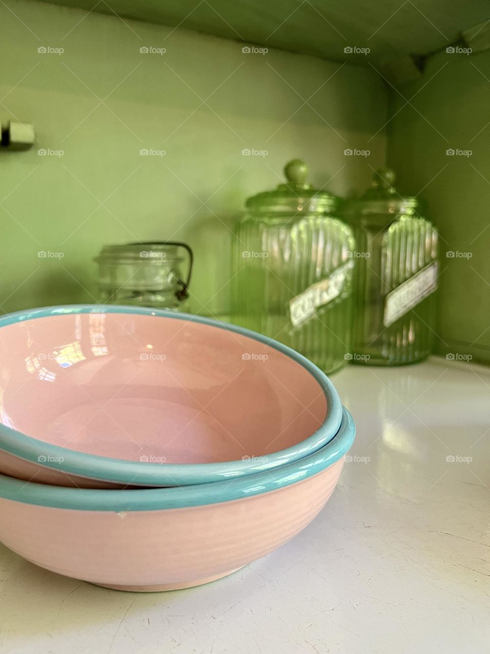Pink ceramic bowls with baby blue rims on an antique green cupboard, with glass containers in the background 