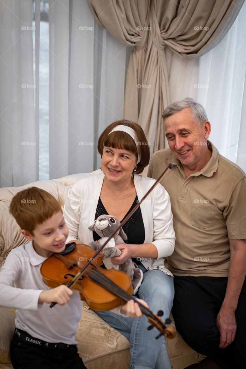 Red-haired boy plays the violin in a bright room, the family listens to music