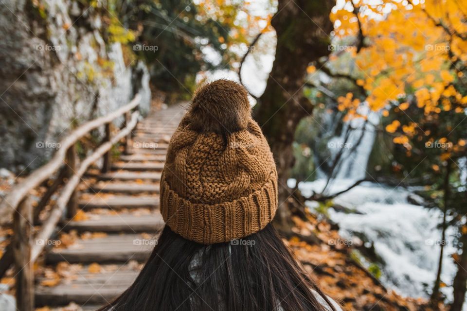 Rear view of woman wearing knitted hat, stanting on path in forest in autumn