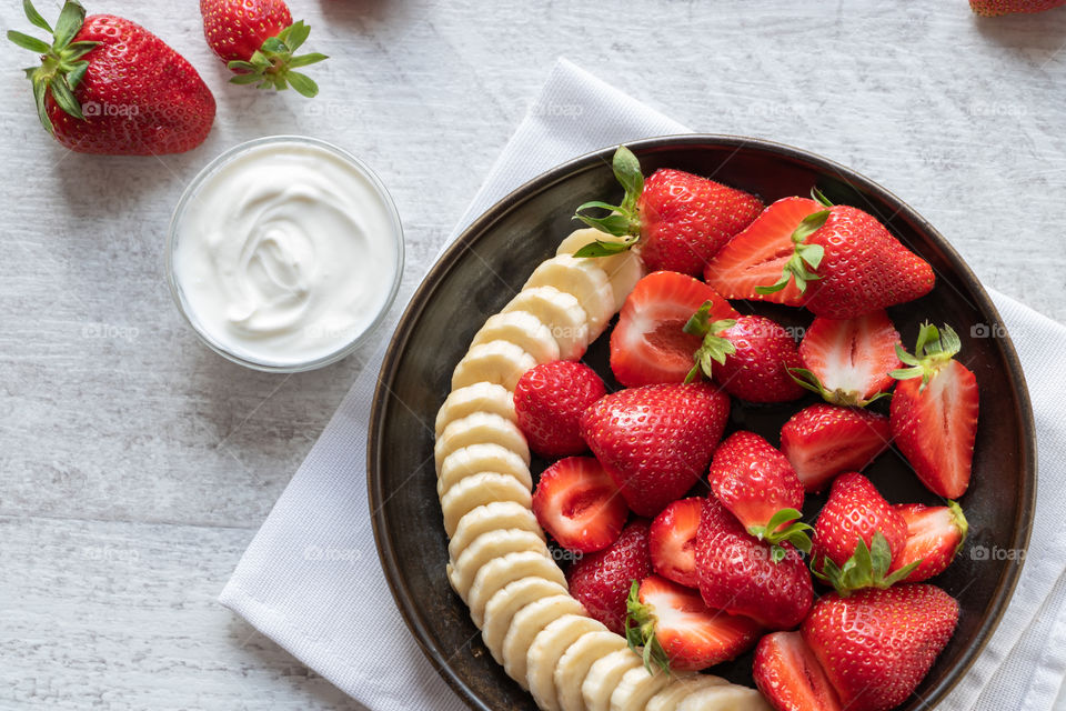 Top view of strawberries and banana salad on wooden table. Concept of healthy lifestyle.