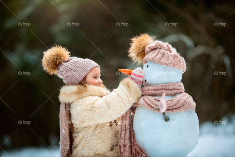 Little girl with snowman in winter forest at sunny day