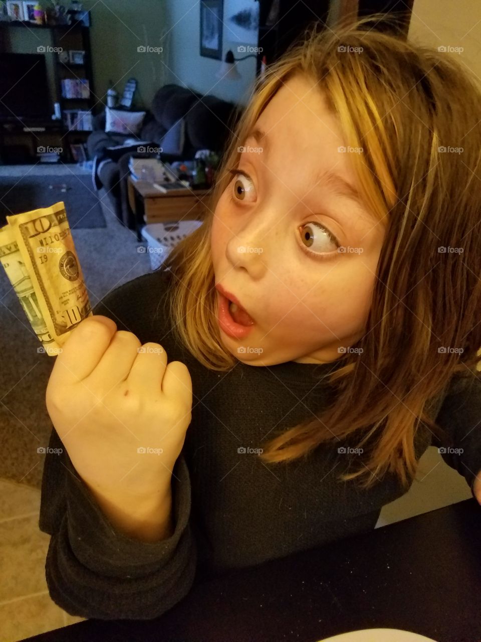 Child amazed at finding a 10 Dollar Bill. She reacts with a wide eye and open mouth.