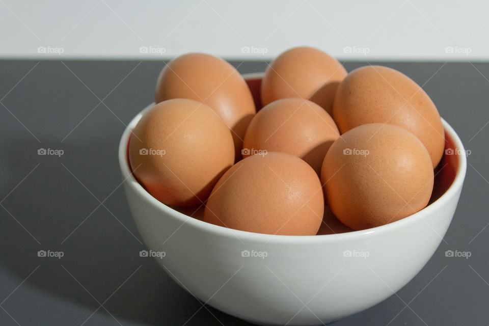 White bowl of brown eggs with white background on grey table