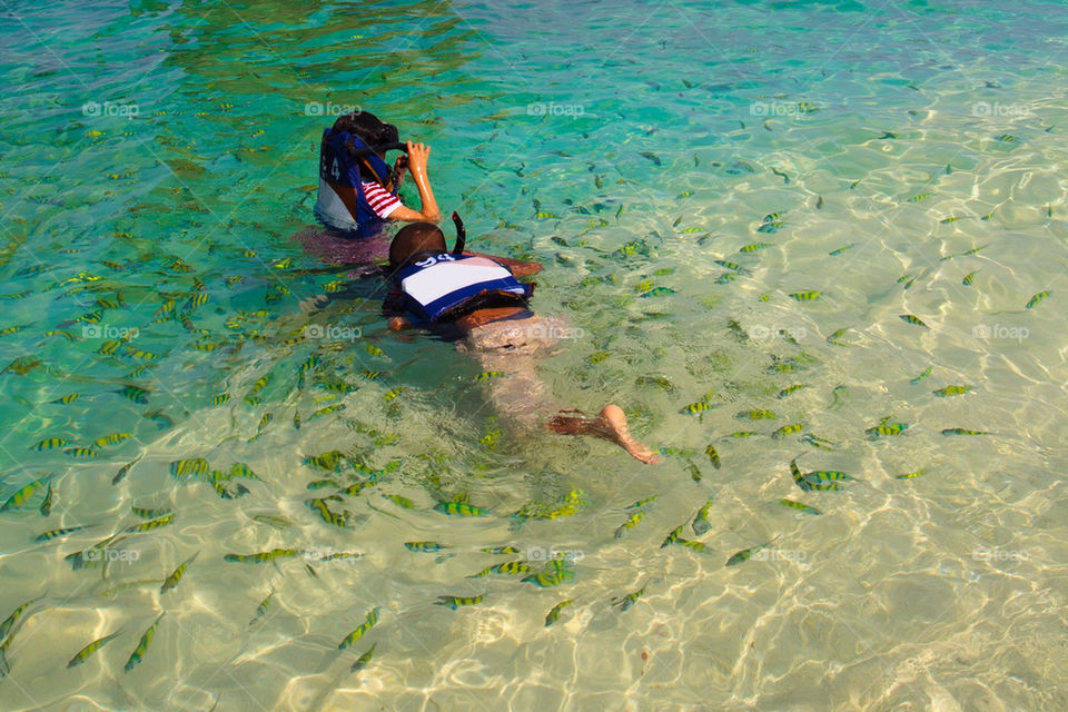 Kids snorkelling in tropical water with lots of fish