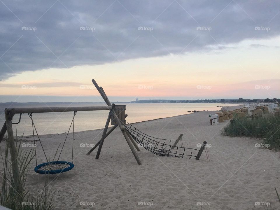 Play structures and swing on the beach during sunrise.