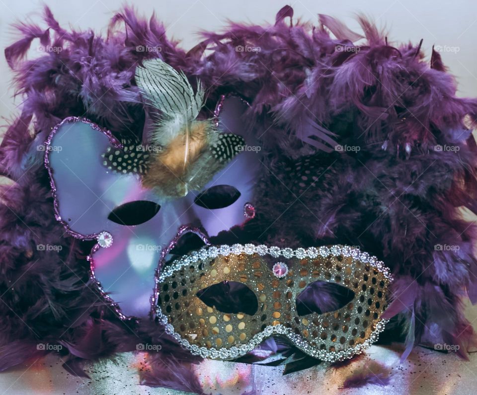 Masquerade style masks displayed with a purple feather boa under disco lights