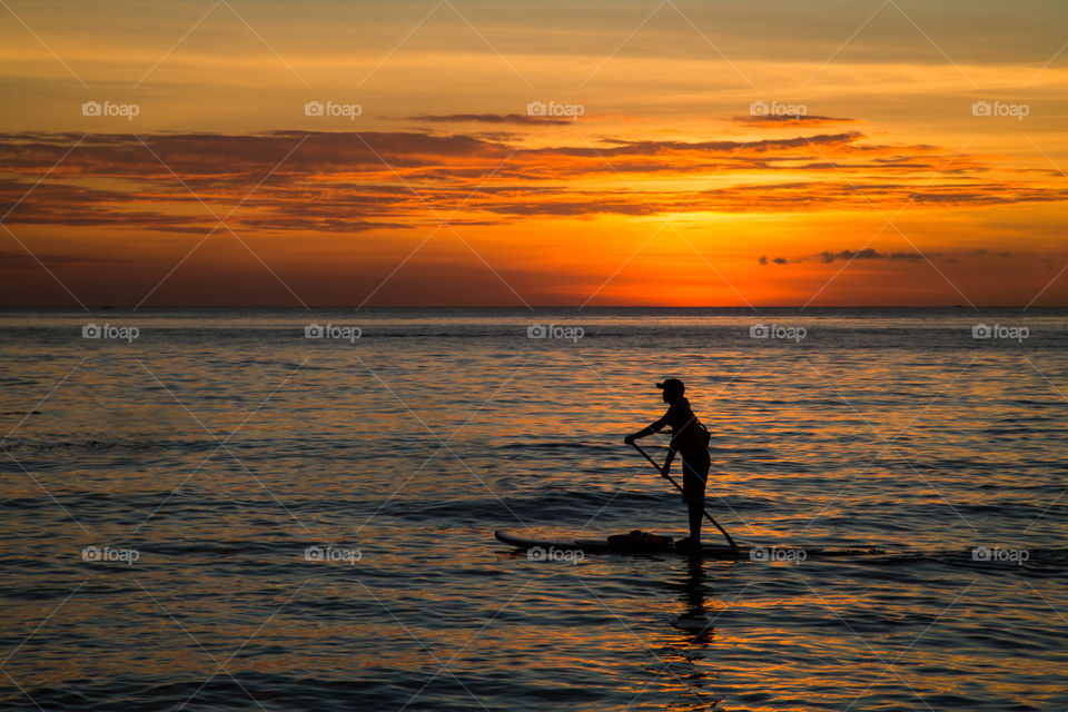 Silhouette of men which using stand up and paddle board on sea