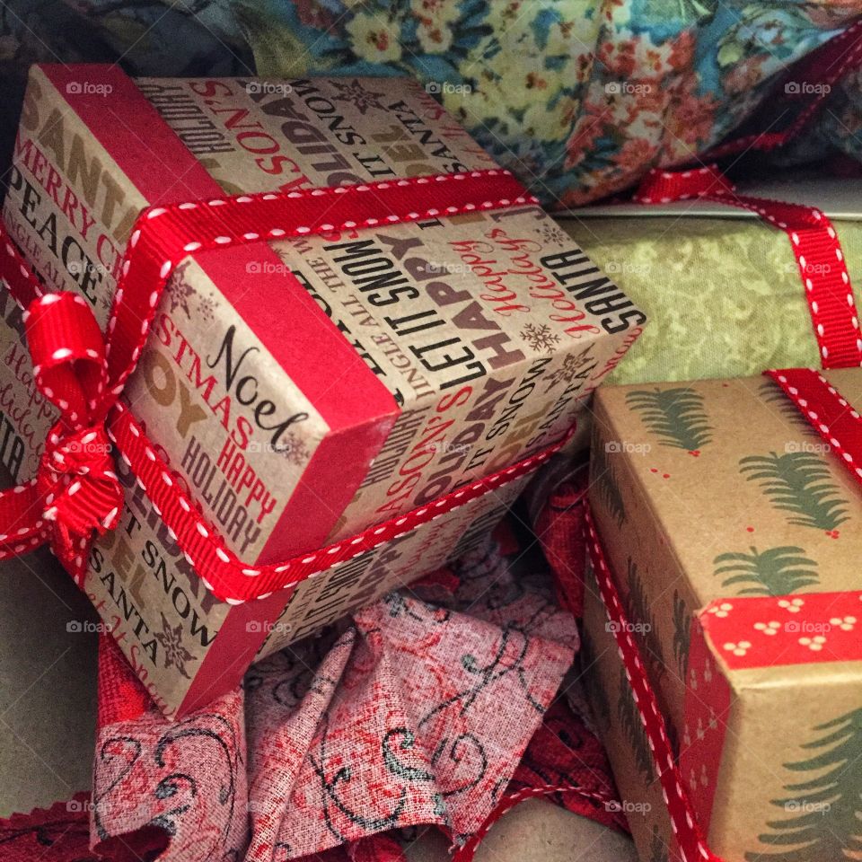 A pile of Christmas boxes tied with ribbon. They are generally read there are also some wrapped presents and cards in the scene. They are wrapped with cloth.