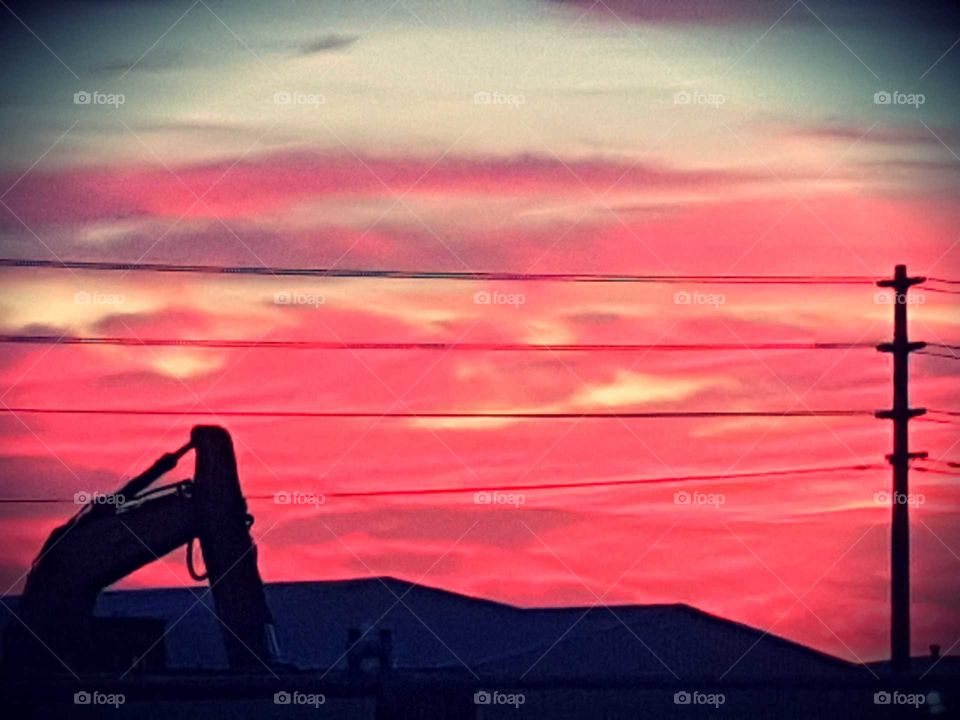 The beautiful sunset over Napier in New Zealand shows stunning natural colors of oranges pinks and yellow. A heavy machine in the background and power lines stand out in black.