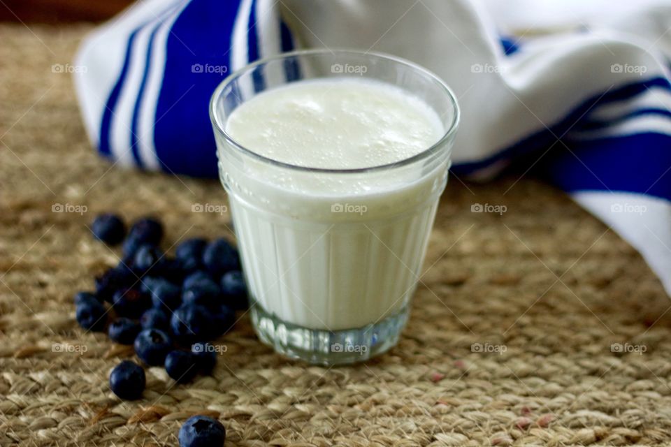 Dairy kefir in a glass, blueberries and a blue-and-white striped dish towel on a natural fiber woven surface