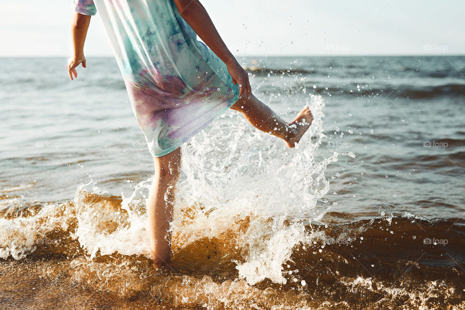 Girl spending a free time jumping splashing in a sea on a beach at sunset during summer vacation