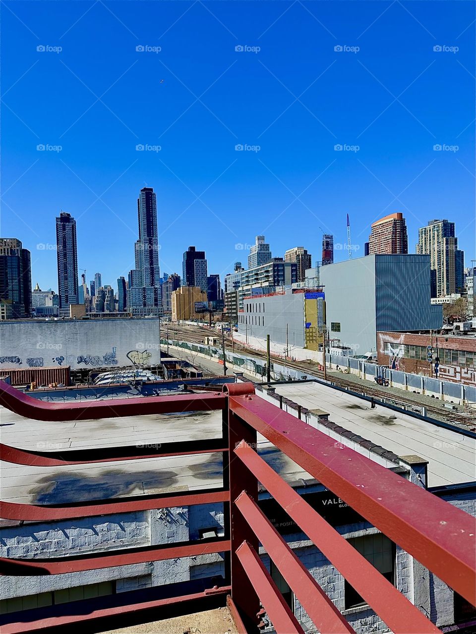 This is the view from the red metal staircase of the “Pulaski Bridge” at “Newtown Creek” in LIC, Queens one story up. The “Long Island Railroad” train tracks can be seen from here and “iFly”, an indoor flight simulator. 2024. Hypnotic Productions