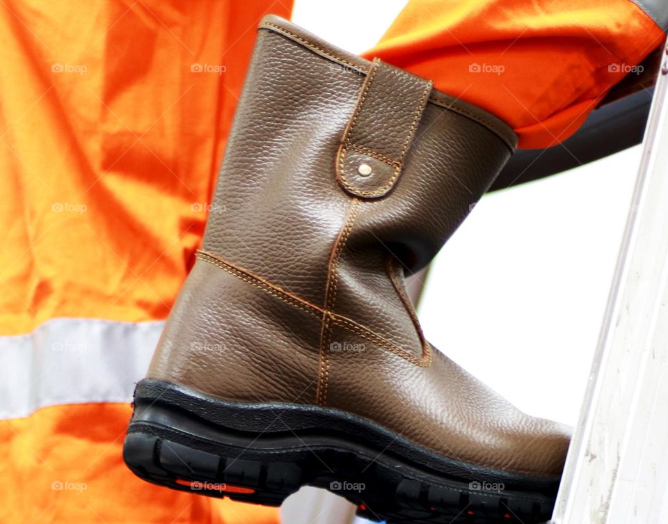 The worker is climbing the stairs, the worker is wearing an orange coverall or clothing and safety shoes