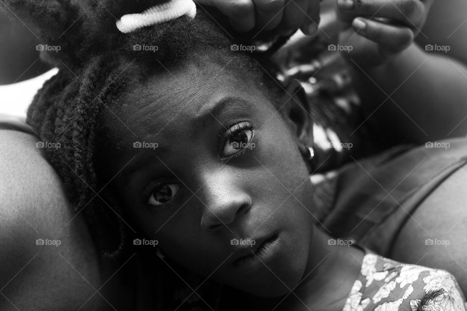 A young female getting her hair done and keeping a neutral emotion as she’s being careful to prevent injury from her hair getting pulled out.