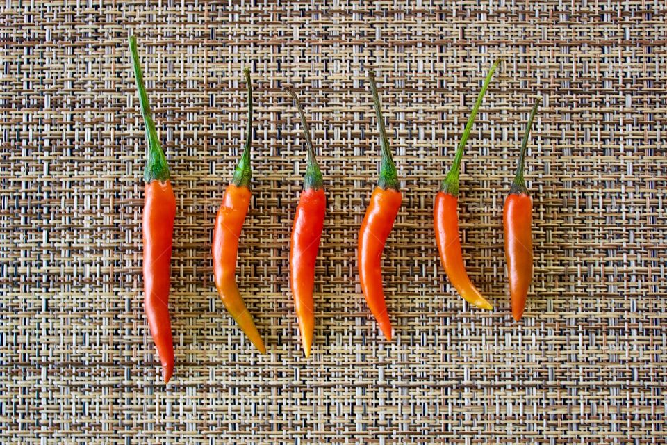 Flat lay minimalistic shot of Thai Bird’s Eye / Thai Bird Chili peppers arranged by size on a woven neutral background