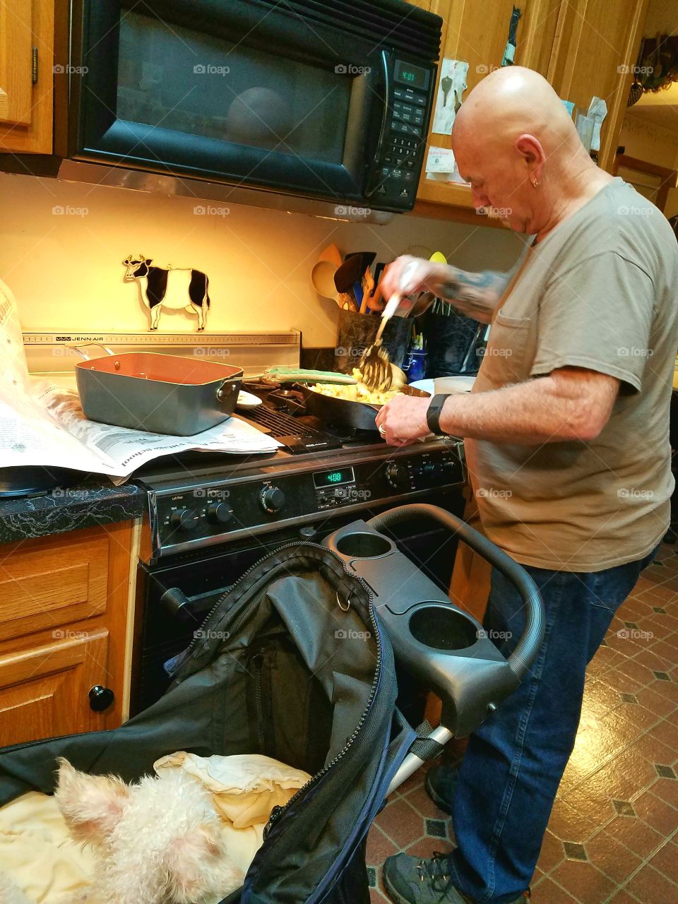 Dog in carriage watching owner cooking in kitchen.