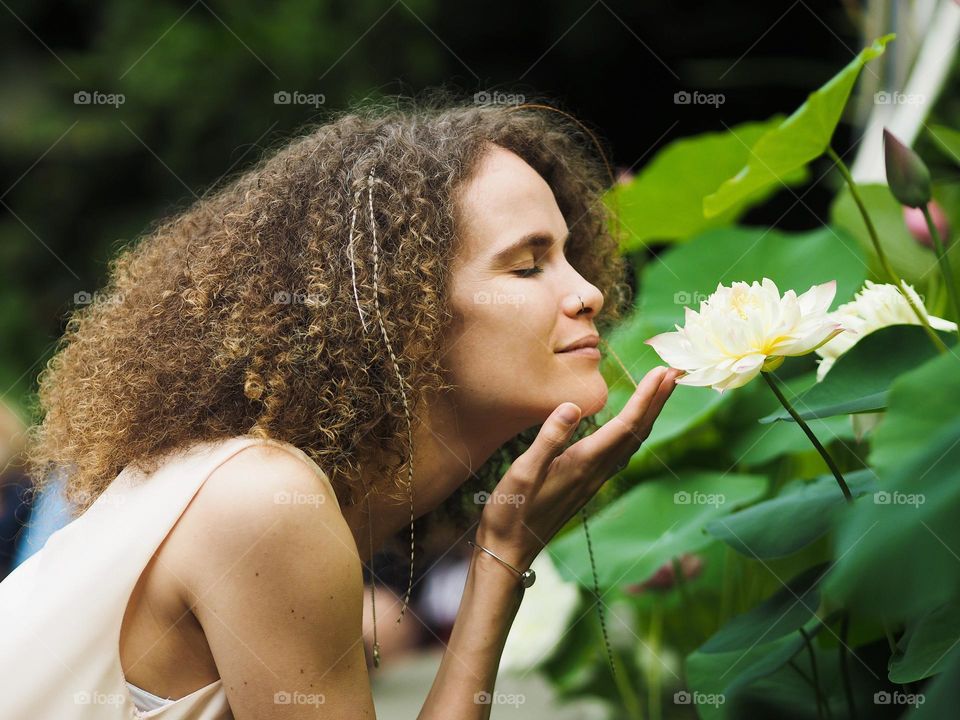 Beautiful young girl with curly hair smelling a lotus flower in a botanical garden, portrait of woman 