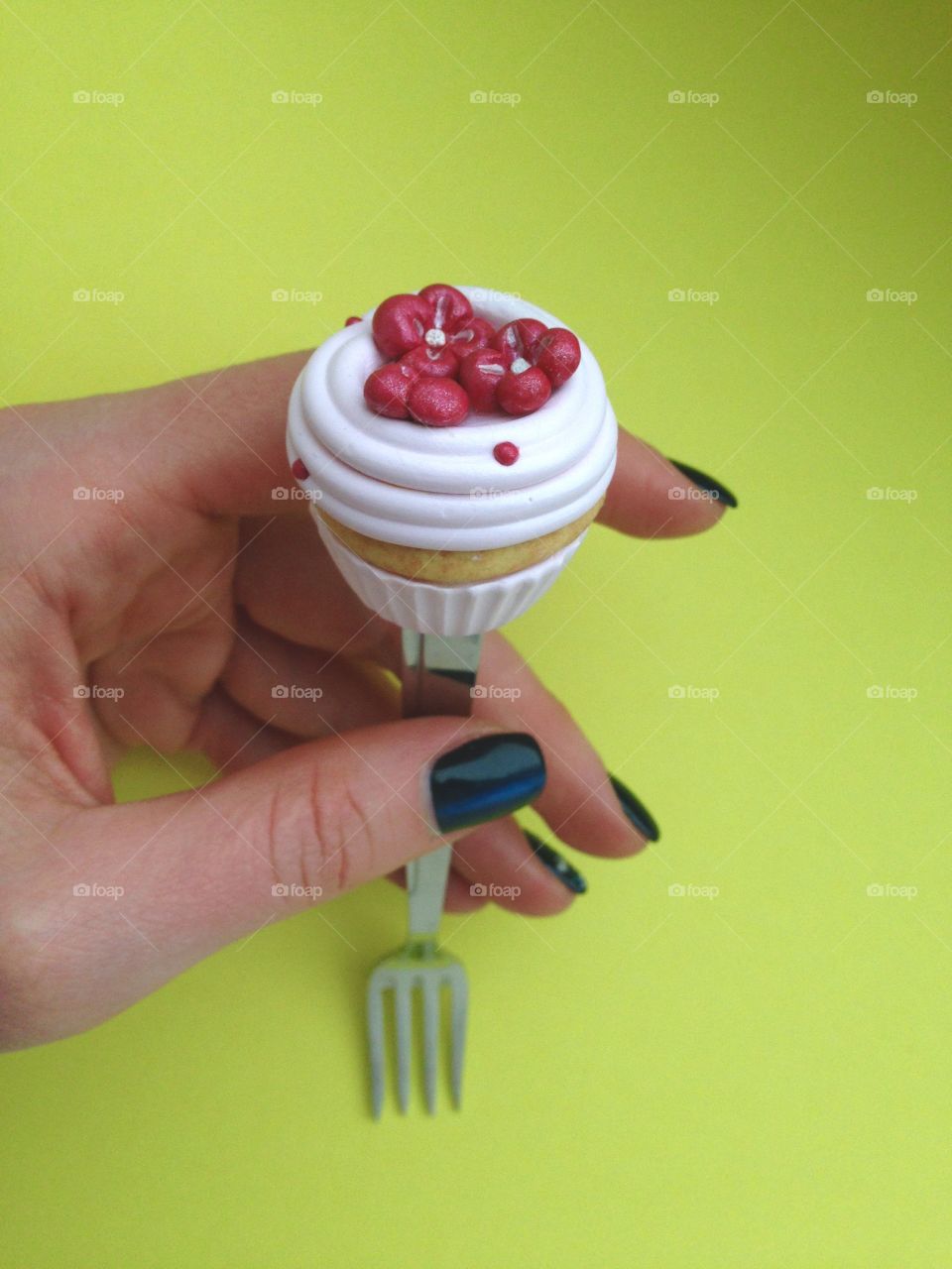 Hand holding a Fork with cupcake on top on yellow background 