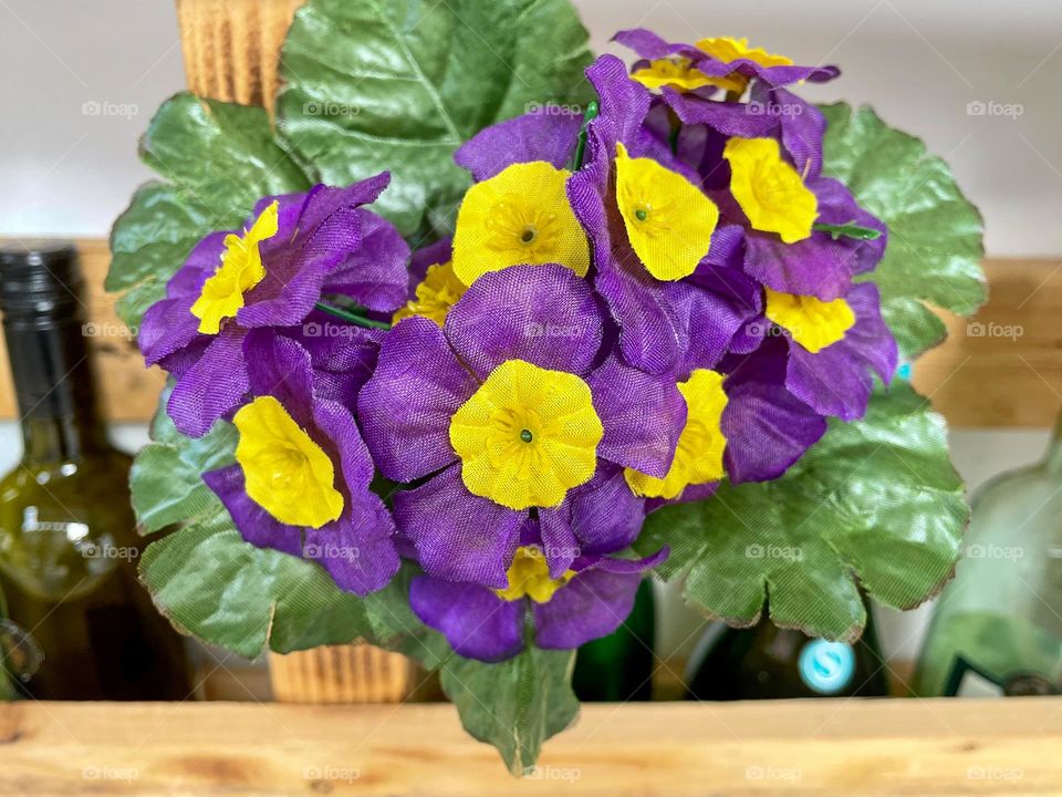 Purple artificial primrose flower on a wooden shelf.