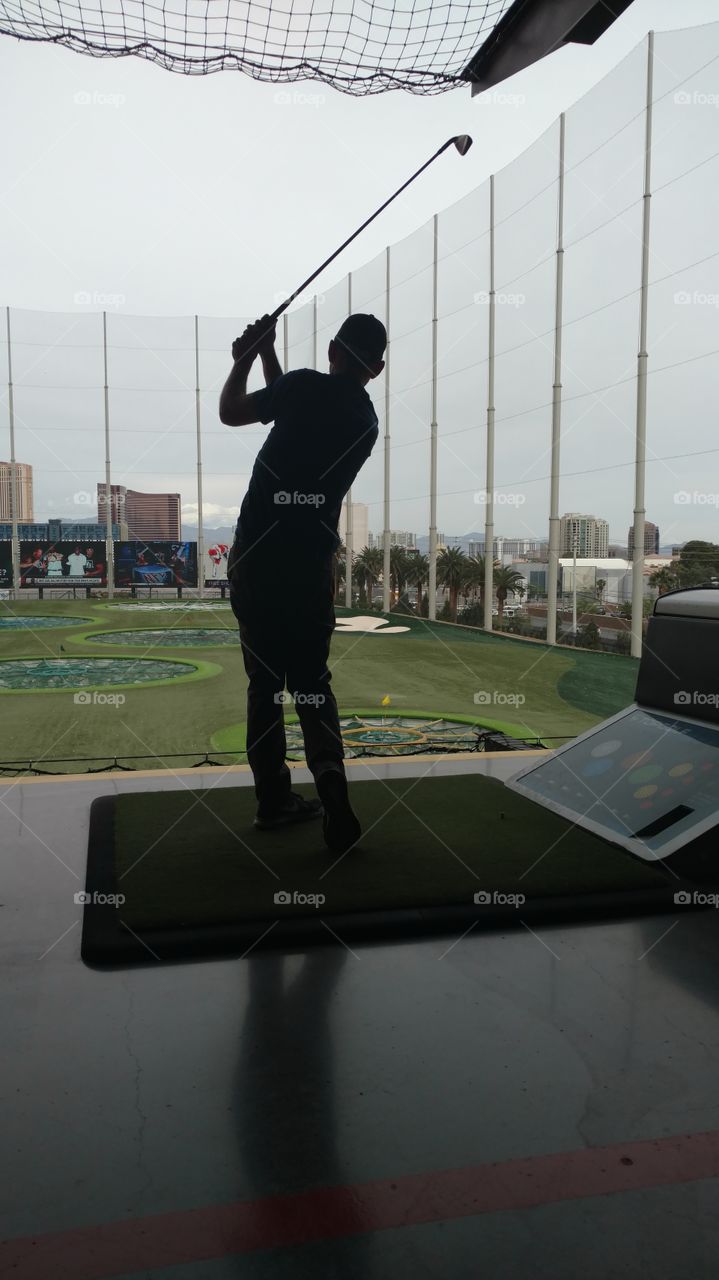 Amateur golfer follows through on a swing from a modern tiered driving range.