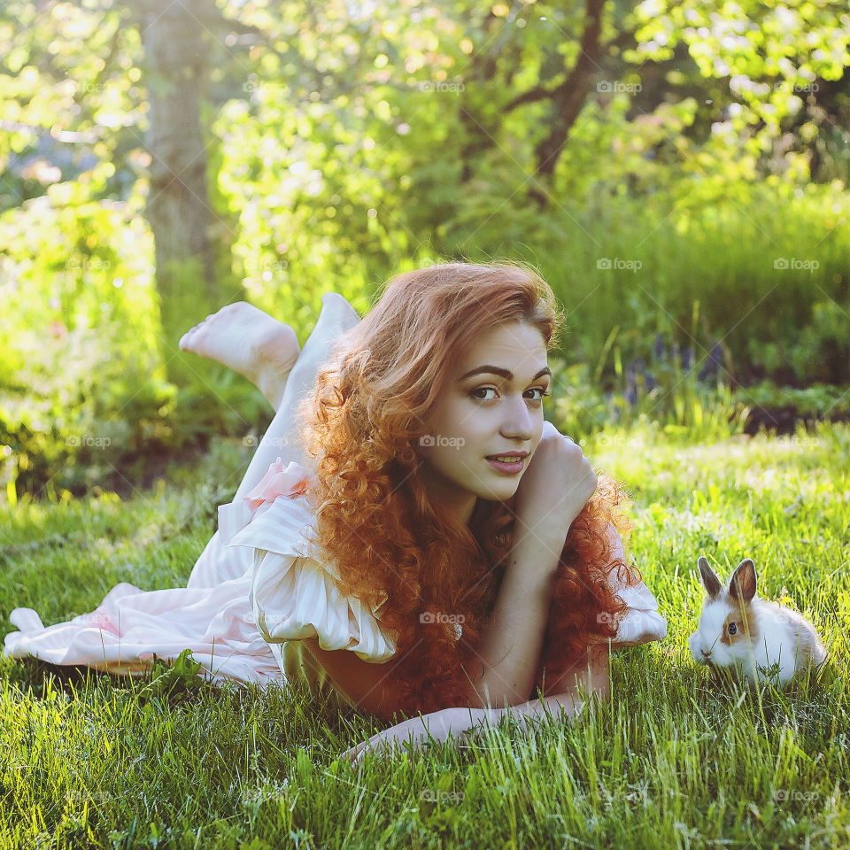 Funny redhead woman playing with rabbit in the sunny day in spring. Lifetime. Outdoor activities