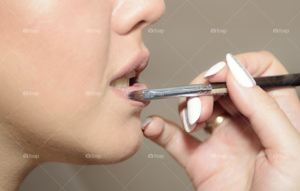 Makeup artist makes makeup to the bride. Beautiful, healthy skin. The lips are painted with natural lipstick. In the hands of the makeup artist a lip brush.