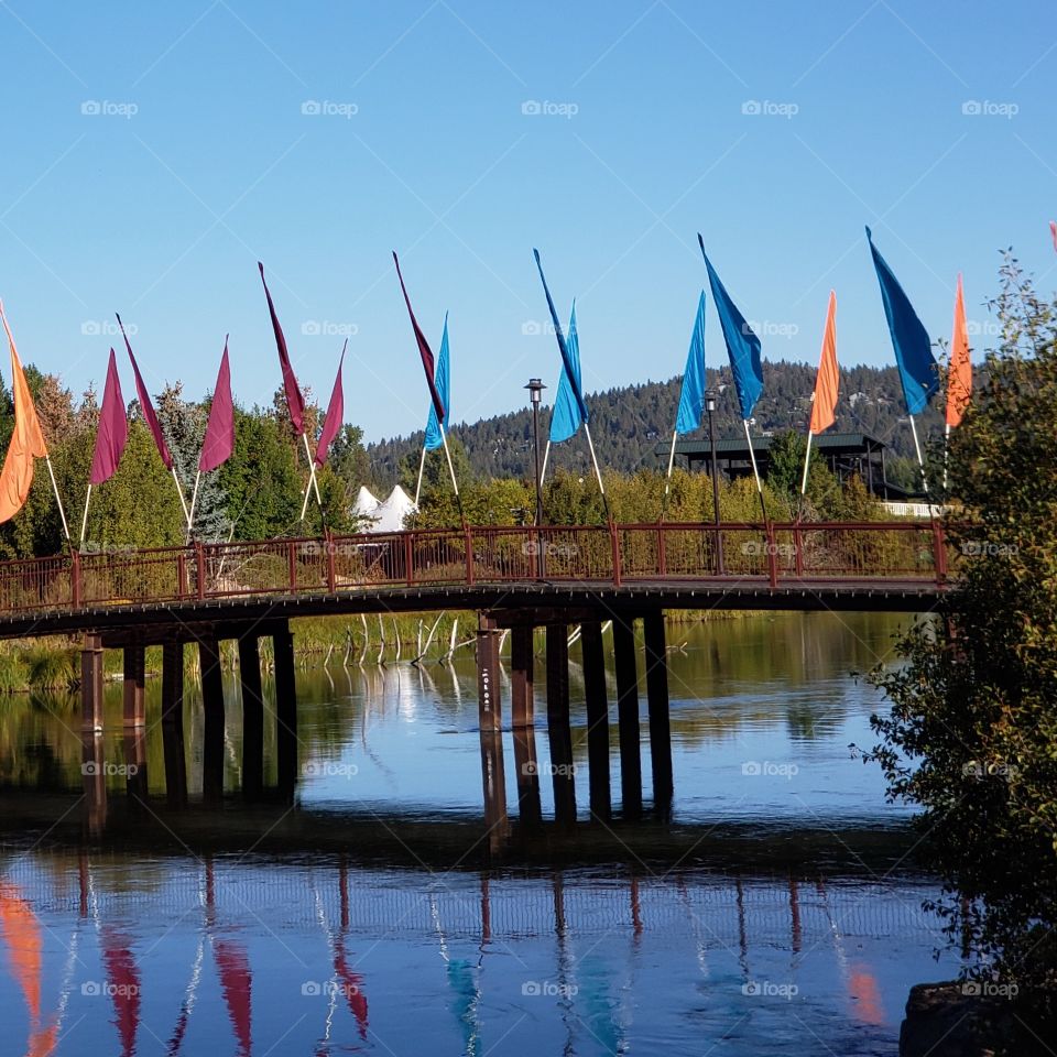 The wooden walking and biking bridge decorated with blue, orange, and pink flags in Bend’s Old Mill District on a beautiful fall morning in Central Oregon. 