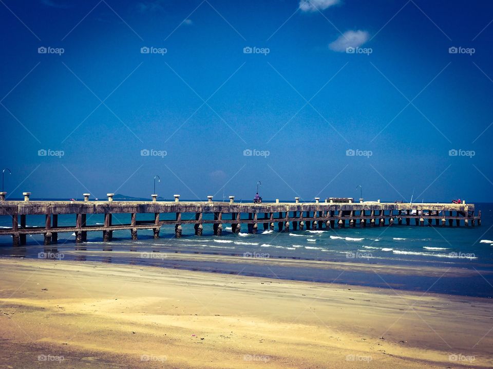 Old concrete pier stretching out from the beach into the turquoise sea at coastal seashore of Thailand