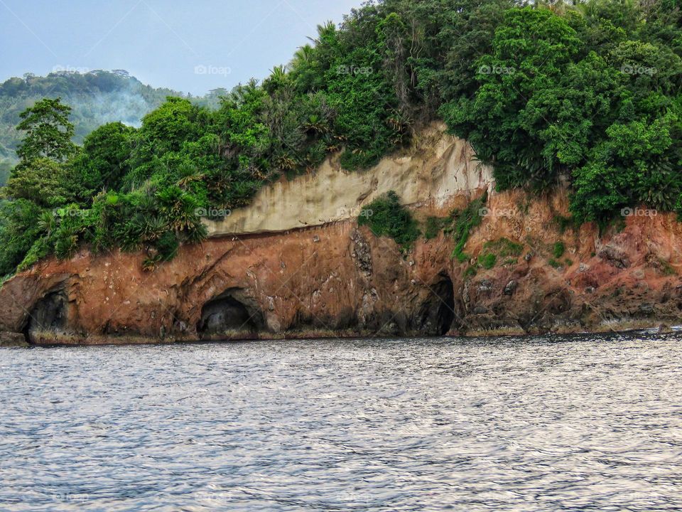 Natural scenery, cliff beaches with beautiful red and white rocks, and green trees, there are three holes at the bottom of the cliff.